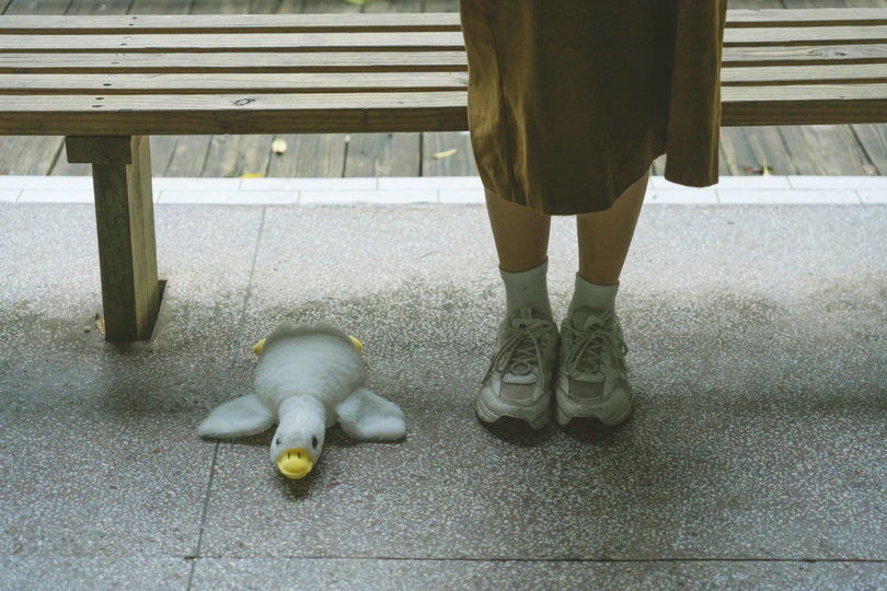 一个人站在人行道上 双脚放在木凳上 旁边有一个毛绒玩具和香蕉。