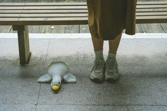 一个人站在人行道上 双脚放在木凳上 旁边有一个毛绒玩具和香蕉。