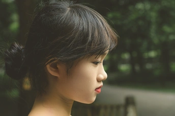 一个穿着连衣裙的年轻女子坐在公园长椅上 身后有树木。