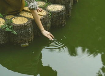 一位年轻女子站在水边 她的手触摸着水面。