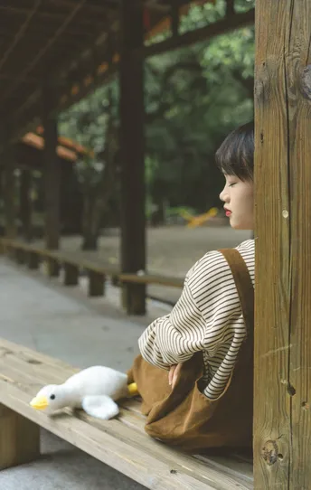 一个年轻女子坐在木凳上 正在看一只小鸭子。