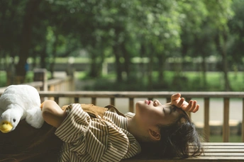 一个年轻女孩在公园的木凳上躺着 凳子上有一个毛绒玩具。