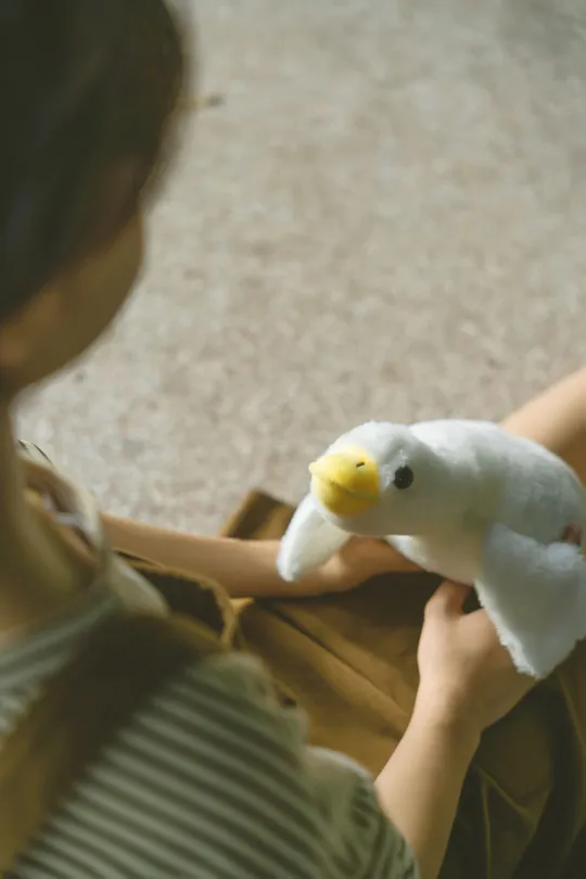 一个年轻女孩抱着一只白色鸭子 而一个妇女在地板上玩着一只填充玩具。