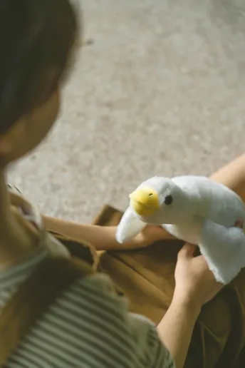 一个年轻女孩抱着一只白色鸭子 而一个妇女在地板上玩着一只填充玩具。