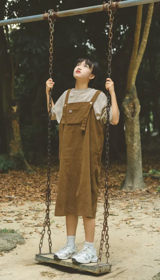 一个公园里的小男孩或小女孩站在秋千上