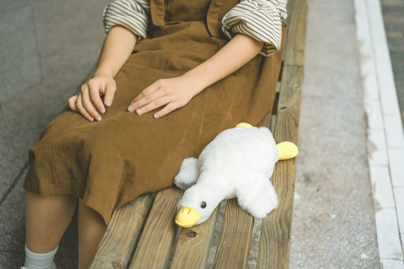 一个年轻男孩坐在木凳上 旁边站着一个穿着裙子的小女孩 手里拿着一个毛绒玩具。