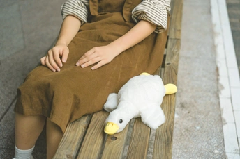 一个年轻男孩坐在木凳上 旁边站着一个穿着裙子的小女孩 手里拿着一个毛绒玩具。