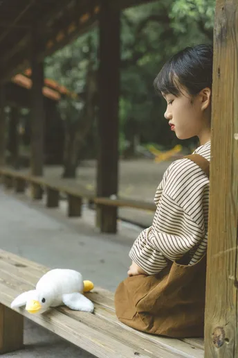 一个年轻男孩坐在木凳上 正在看一个小毛绒动物和一只鸭子。