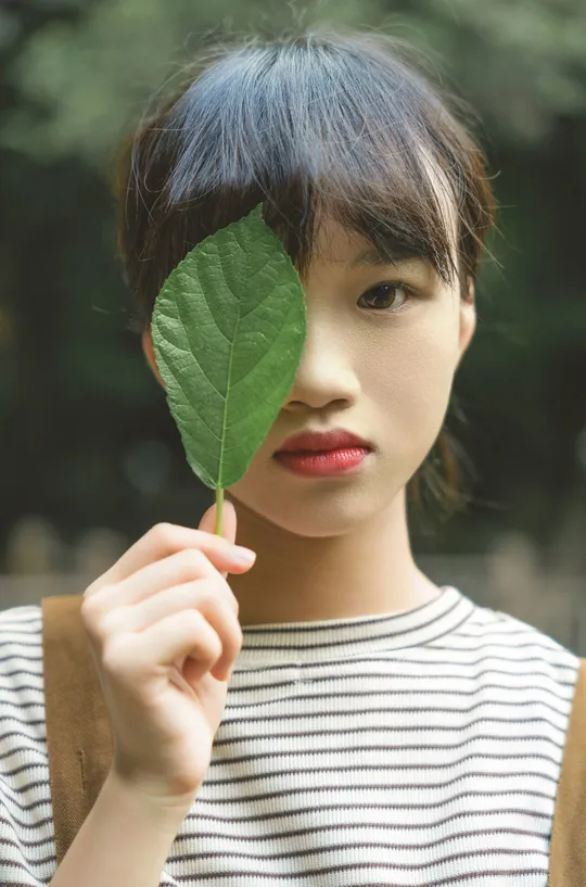 一位年轻女子举着一片绿叶挡在面前
