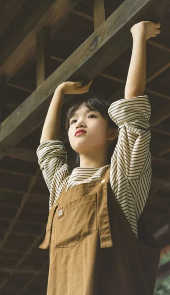 一位穿着棕色连体衣的年轻女子站在那里 双手背后 双臂在头上。