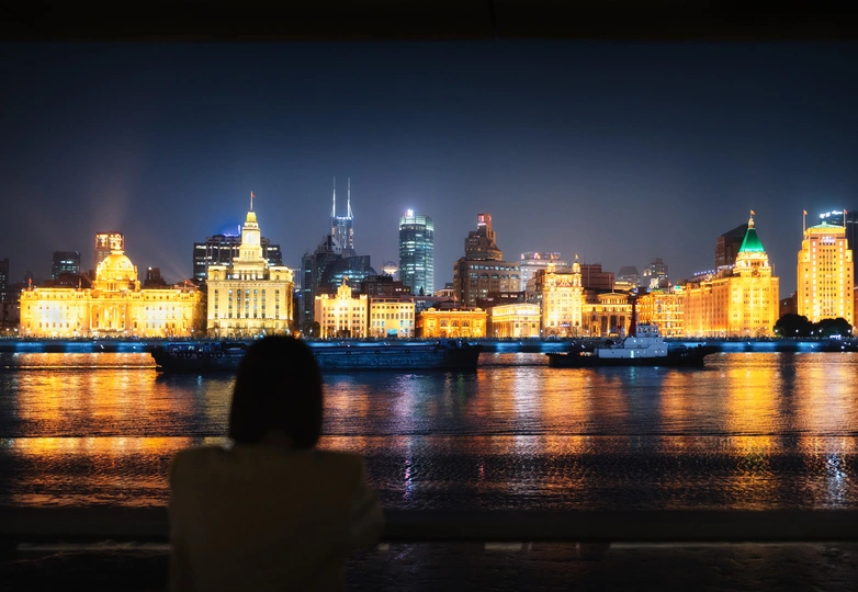 一个人坐在长凳上 眺望着夜晚的城市轮廓 被灯光照亮。