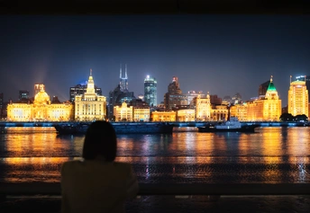 一个人坐在长凳上 眺望着夜晚的城市轮廓 被灯光照亮。