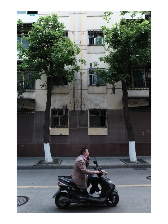 一名男子骑着摩托车在大楼前的街道上打电话