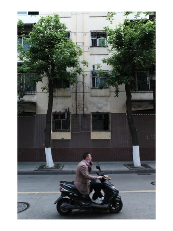 一名男子骑着摩托车在大楼前的街道上打电话