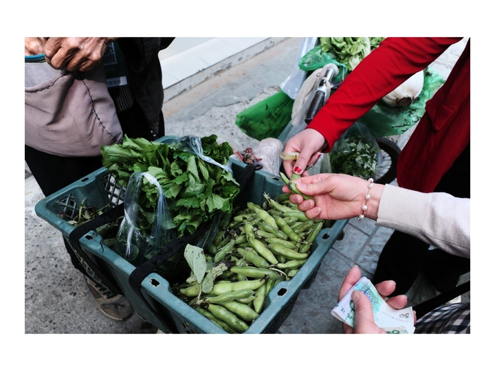 在市场上 一名妇女把手伸进一盒新鲜的绿豌豆里 背景是其他几箱食物