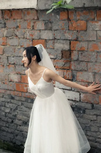 一位穿着白色婚纱站在砖墙前的女人