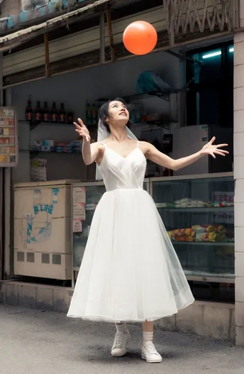 一位穿着白色连衣裙的年轻女子拿着一个橙色球