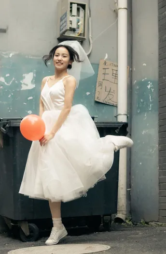 一位穿着白色连衣裙的年轻女子在街上拿着一个橙色气球。