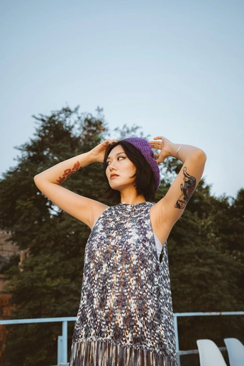 一位穿着连衣裙和紫色帽子的年轻女子站在外面 双手抱头