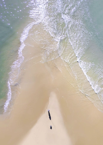 一个人在沙地上行走 一艘船在水里站着。
