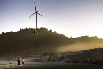 直升机在沙滩上飞越风力发电机