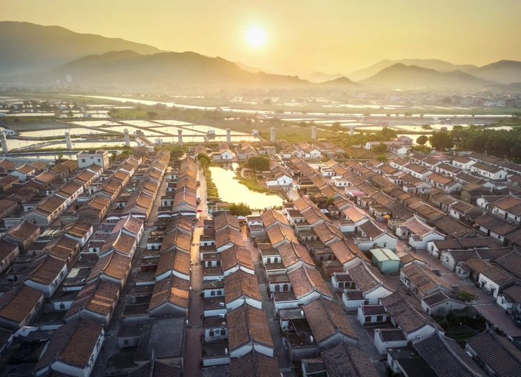 夕阳或日出时 带有房顶的村庄和背景中的山脉的 aerial view