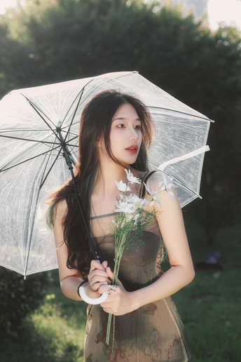 一位穿着连衣裙的年轻女子手持透明雨伞和白色花朵