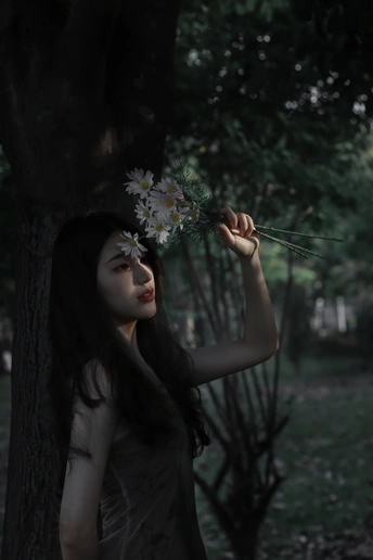 一位年轻女子手持一朵花在森林中