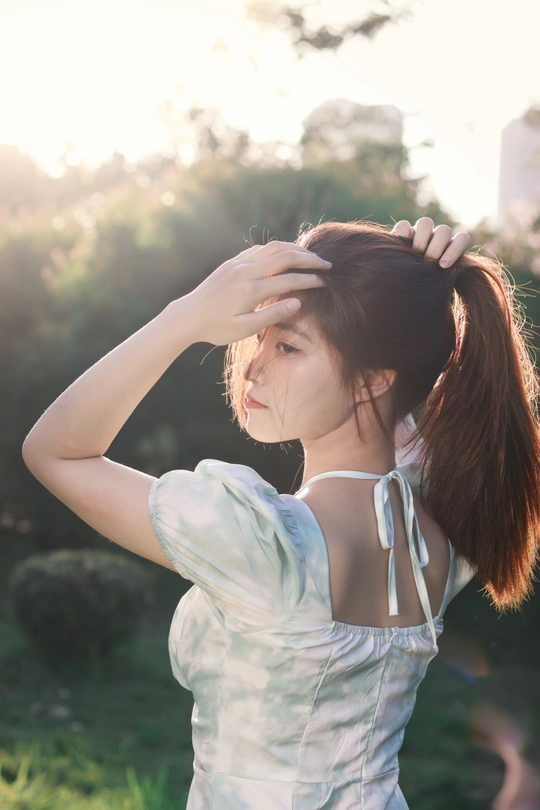 一个穿着白色连衣裙的年轻女子站在外面 双手背后 马尾发型。