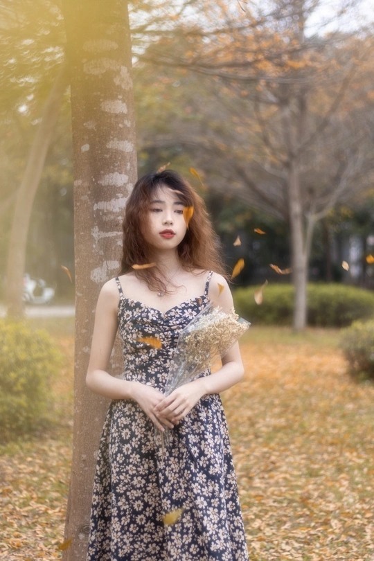 一位穿着连衣裙的年轻女子靠在公园中的一棵树上