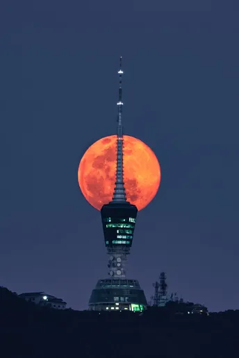 a red moon rises behind a building