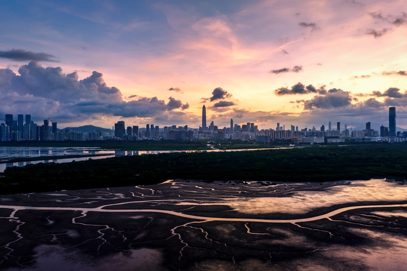夕阳下的城市天际线 太阳低垂在天空中 前景是一条河流。
