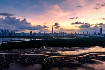 夕阳下的城市天际线 太阳低垂在天空中 前景是一条河流。