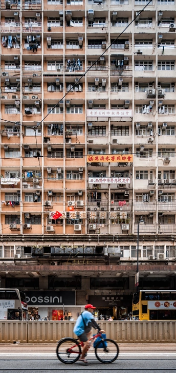 一个人骑自行车穿过大型城市中的一座高楼大厦前的街道。