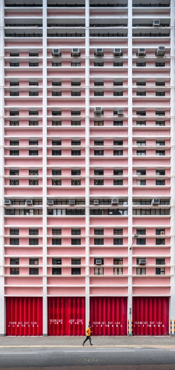 一位妇女在城市中走过一座高楼 而一个男子正在街上骑车。