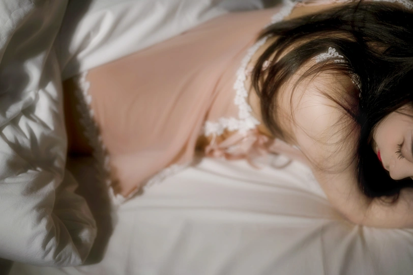 一个穿着白色连衣裙的年轻女子躺在铺着床单的床上