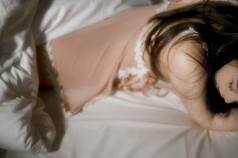 一个穿着白色连衣裙的年轻女子躺在铺着床单的床上