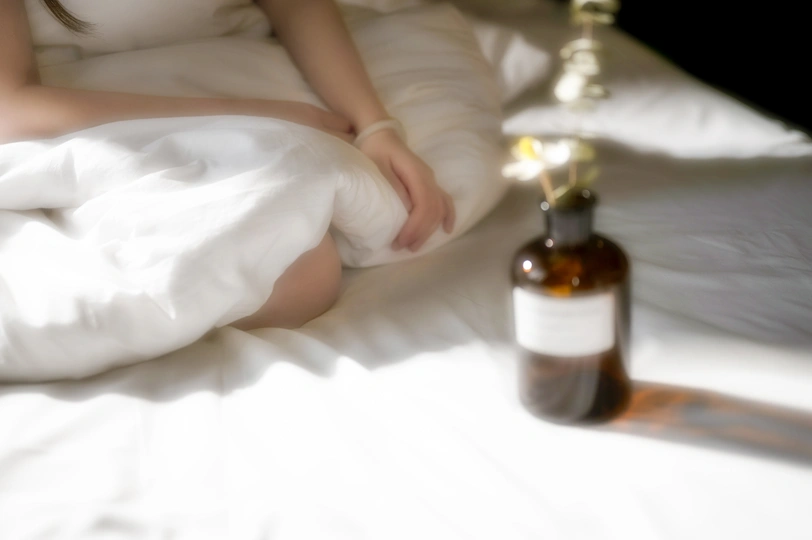 一个女人躺在床上 手里拿着白色床单和一瓶葡萄酒