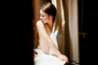 一个穿着白色连衣裙的年轻女子站在房间的窗户前