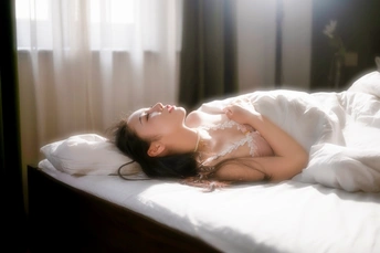 一个年轻女人躺在窗户旁边的一张铺着白色床单的床上