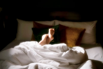 一个人躺在床上 白色床单和枕头 双脚向上 枕头上放着一本书