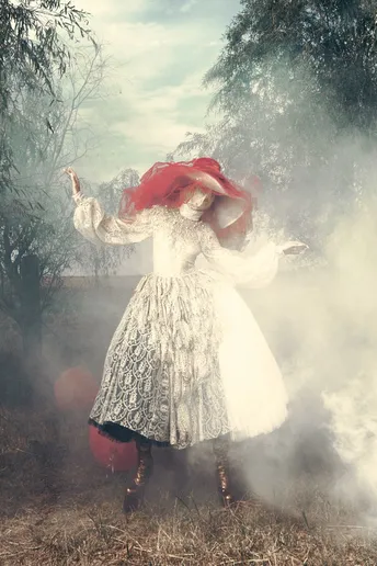 一位穿着白色连衣裙和红色帽子的女人站在一个田野里 手里拿着一把红色雨伞。