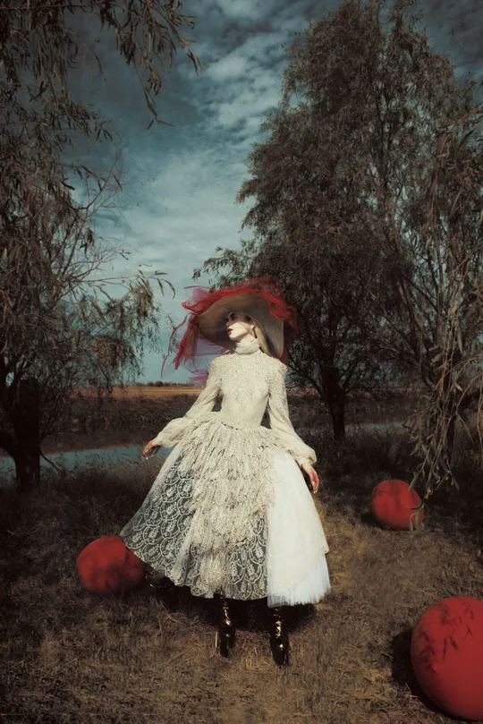 一幅穿着白裙和帽子 手持红色雨伞站在田野中的女人画像。