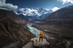 一个男子和他的狗站在一块俯瞰蓝色河流和山峦的岩石上