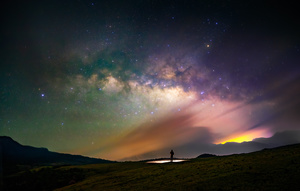 一个人站在一个 hill 上 在星空下 星星闪烁。