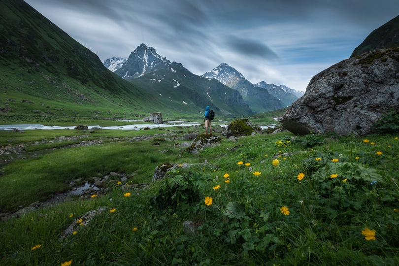 站在绿草地上 周围有巨大的岩石和鲜花 远处有山脉。