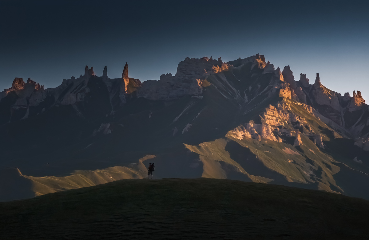 一个人站在山顶 背景是照亮的山脉 月亮照亮了它。