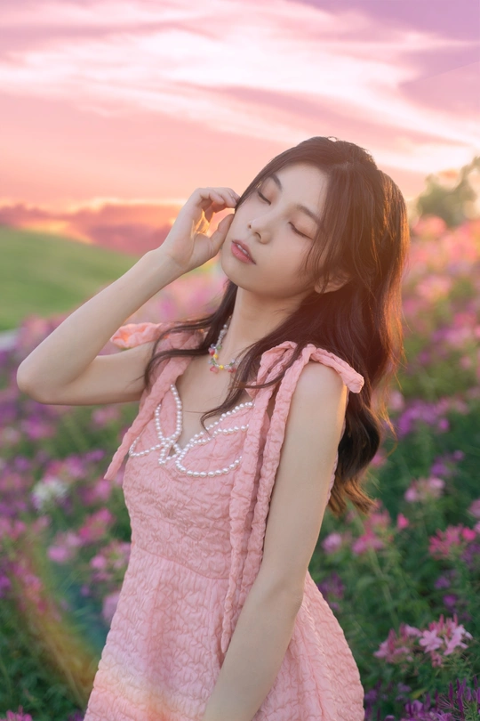 一个穿着粉红色裙子的年轻女子站在夕阳下的花田中