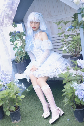 一个蓝头发、穿着白色连衣裙的女孩坐在花园里的长椅上 花园里种着盆栽植物