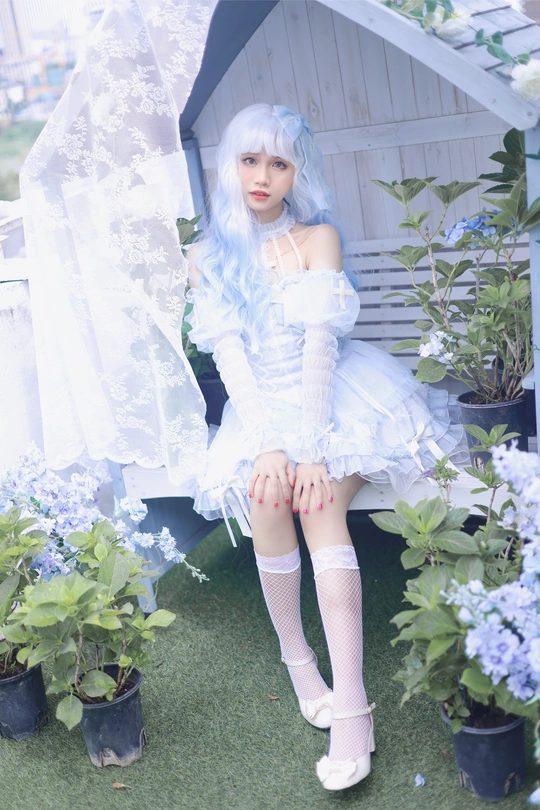 一个蓝色头发、戴着白色假发的娃娃坐在外面的盆栽和鲜花旁边